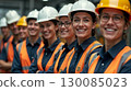 Group of smiling construction workers wearing safety helmets and reflective vests standing together in an industrial environment. 130085023