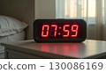 Close-up of a red LED digital alarm clock showing 7:59 on a nightstand in the morning 130086169