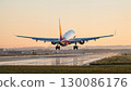 Rear view of a commercial airplane touching down on a wet runway at sunrise, with smoke coming from the tires. 130086176