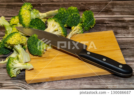 A close-up shot of fresh broccoli florets being prepared on a wooden cutting board with a chef's knife on a rustic wooden table. 130086687