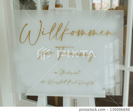 Elegant welcome sign for a wedding displayed on an easel at the venue entrance. Gold cursive writing adds a touch of sophistication, welcoming guests to the special event Elegant welcome sign for a wedding displayed on an easel at the venue entrance. Gold cursive writing adds a touch of sophistication, welcoming guests to the special event 130086698