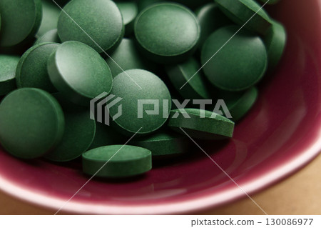 Green spirulina pills in red bowl. Nutrition detox supplement. Macro shot.  130086977