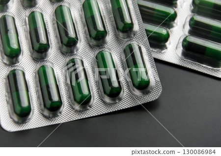 Foil blister pack of pharmaceutical natural herbal green capsules on black ceramic background. Close-up Foil blister pack of pharmaceutical natural herbal green capsules on black ceramic background. Close-up 130086984