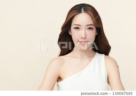 A beautiful young Asian woman with clean, fresh skin against a beige background. Skincare, facial treatment, cosmetology, beauty, and spa. An elegant portrait of an Asian woman. 130087085