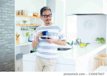 Lifestyle: A middle-aged man standing in the kitchen holding a coffee cup 130087607
