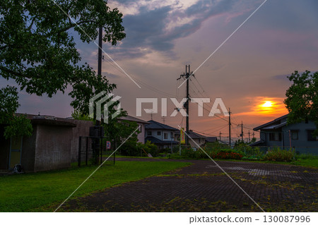Late summer: A golden sunset peeking through the clouds, enveloping the cityscape beyond the park in the glow of the setting sun. Late summer: A golden sunset peeking through the clouds, enveloping the cityscape beyond the park in the glow of the setting sun. 130087996