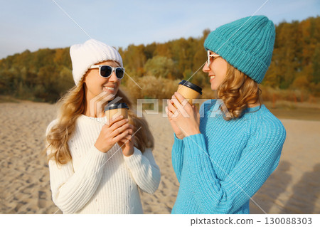 Happy young women friends talking with coffee drinks on beach, smiling girlfriends together on sea 130088303