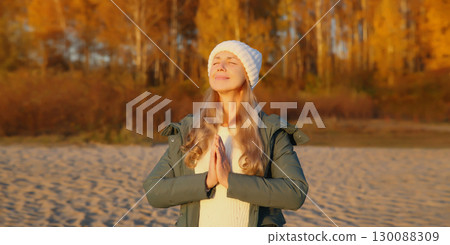 Calm relaxed healthy young woman meditates in autumn park on sea beach against trees 130088309