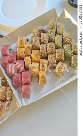 Assorted sushi rolls with tuna, avocado, and sesame served in a paper tray. Japanese cuisine concept, representing variety, freshness, and gourmet takeaway 130088581