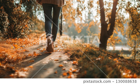 The feet of a woman walking along a tree-lined path in autumn 130088638