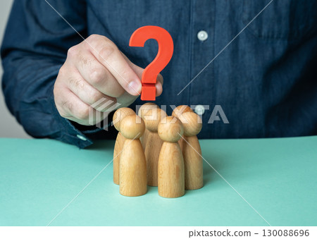 A man holds a question mark over a group of people figurines. To set the agenda. To find out the opinion of the team. To confuse the people and create uncertainty 130088696