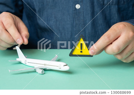 A man holds a sign of attention near a passenger plane. Some problems or malfunctions that risk canceling the flight, causing delays and safety concerns 130088699