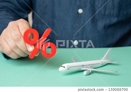 A man holds a red percentage near a passenger plane. Rising prices for flights. Taxes and fees. Debts of airlines and economic pressure on aviation A man holds a red percentage near a passenger plane. Rising prices for flights. Taxes and fees. Debts of airlines and economic pressure on aviation 130088700