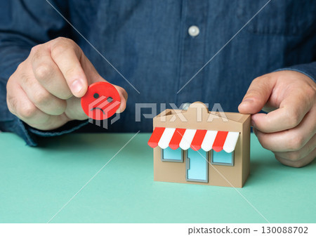 A man holds a sad smiley near a store. Bad review. Not happy with the service, reflecting poor customer experience and negative reputation impact 130088702