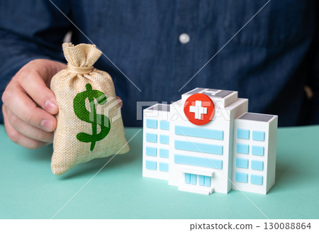 Man holding dollar money bag near hospital building. Investments in medicine, charity fund. Healthcare funding, budget. 130088864