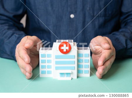 A man protects a hospital building with his hands. Concept of protecting the healthcare system. Medical security, patient safety, public health protection A man protects a hospital building with his hands. Concept of protecting the healthcare system. Medical security, patient safety, public health protection 130088865