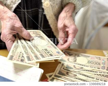一位老婦人在存摺前數著許多萬日元鈔票 一位老婦人在存摺前數著許多萬日元鈔票 130089218