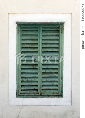 Close-up view of a rustic green shuttered window set within a worn white wall Close-up view of a rustic green shuttered window set within a worn white wall 130090074