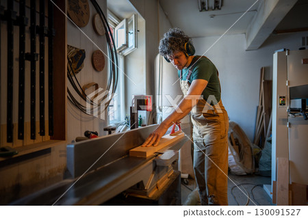 Skilled woodworker operate jointer machine, process wooden beam with power tools in workshop Skilled woodworker operate jointer machine, process wooden beam with power tools in workshop 130091527