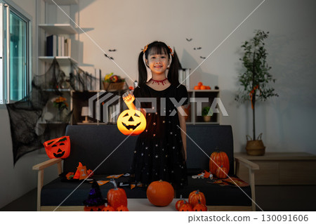 Halloween Joy. Young girl holding a glowing pumpkin lantern, celebrating Halloween spirit. 130091606
