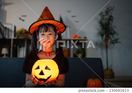 Halloween Costume Fun. Girl in witch hat holding a glowing pumpkin for Halloween. 130091613