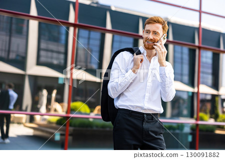 Red-haired man in white shirt holding jacket over shoulder talking on smartphone Red-haired man in white shirt holding jacket over shoulder talking on smartphone 130091882
