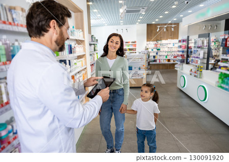 Young mom with a cute kid choosing medicine in the pharmacy, male pharmacist helping her 130091920