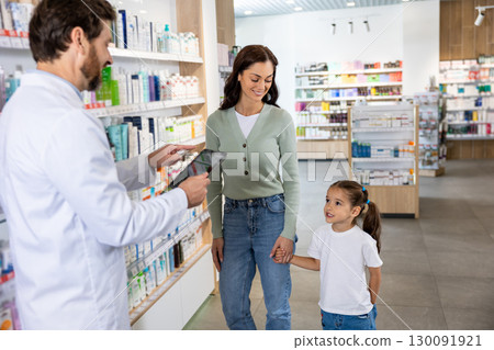 Young mom with a cute kid choosing medicine in the pharmacy, male pharmacist helping her 130091921
