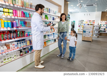 Young mom with a cute kid choosing medicine in the pharmacy, male pharmacist helping her Young mom with a cute kid choosing medicine in the pharmacy, male pharmacist helping her 130091923