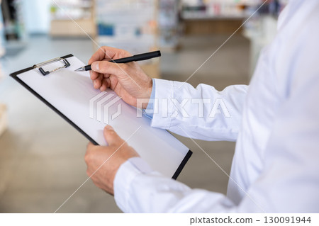 Close up picture of a man in lab coat making notes 130091944