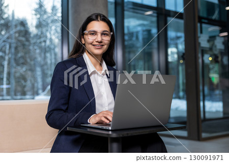 Dark-haired woman in eyeglasses working on laptop and looking confident Dark-haired woman in eyeglasses working on laptop and looking confident 130091971