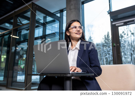 Dark-haired woman in eyeglasses working on laptop and looking confident Dark-haired woman in eyeglasses working on laptop and looking confident 130091972