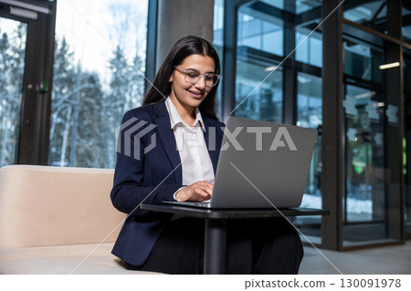Dark-haired woman in eyeglasses working on laptop and looking confident Dark-haired woman in eyeglasses working on laptop and looking confident 130091978