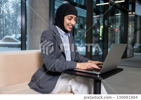 Muslim businesswoman in hijab working on laptop and looking involved 130091984
