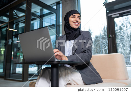 Young woman in hijab working on laptop and smiling Young woman in hijab working on laptop and smiling 130091997