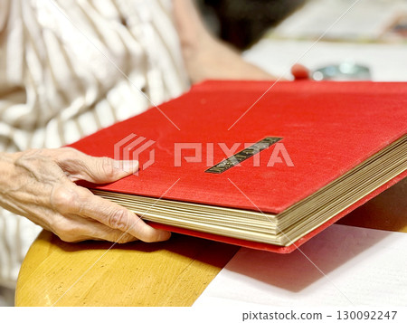 An elderly woman holding an album with a red cover 130092247
