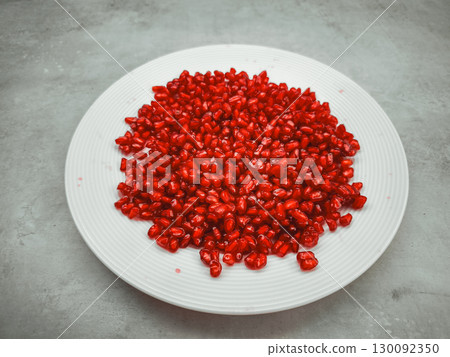 Fresh pomegranate seeds filling a white plate on a gray background 130092350