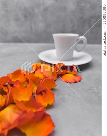 Orange rose petals leading to a white coffee cup on a gray table 130092390