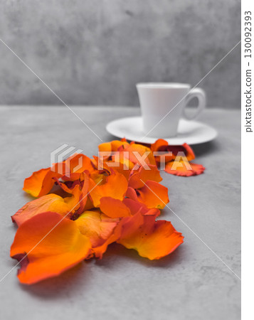Orange rose petals leading to a coffee cup on a gray table 130092393