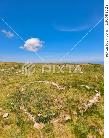Heart shaped stone arrangements on a grassy hillside under a blue sky 130092528