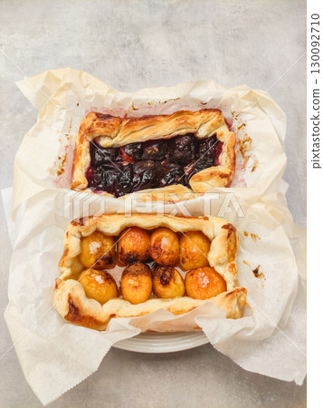 Baking delicious fruit tarts with apricots and plums on parchment paper 130092710