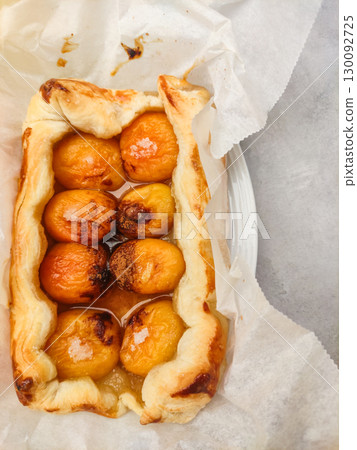 Delicious apricot tart emerging from baking paper on marble surface 130092725