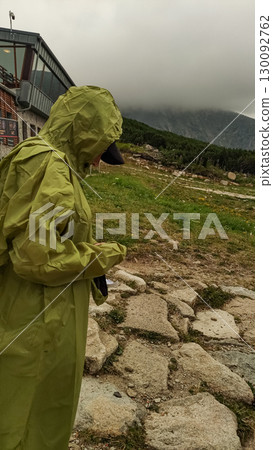 Hiker wearing raincoat standing near mountain lodge in high tatras, slovakia 130092762