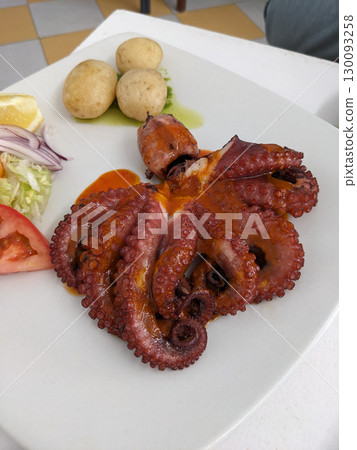 Delicious grilled octopus served with potatoes, salad, and lemon on a white plate, a flavorful dish. 130093258