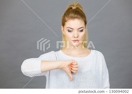 Sad woman showing thumb down gesture 130094002