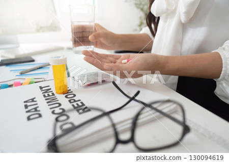Health Awareness. Woman taking medication with water at her desk. Health Awareness. Woman taking medication with water at her desk. 130094619