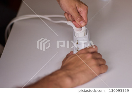 Hands Carefully Connecting a Plug to a Power Strip for Convenient Charging Needs 130095539