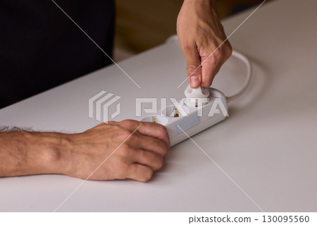 Hands Carefully Connecting a Plug to a Power Strip for Convenient Charging Needs 130095560