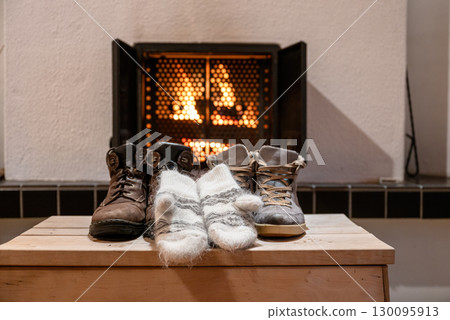 Winter boots and wool mittens drying in front of fireplace indoors cozy home 130095913