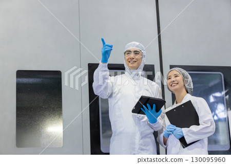 工廠裡穿著防護衣的工人使用平板電腦 工廠裡穿著防護衣的工人使用平板電腦 130095960